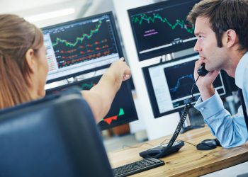 A rearview shot of two concerned stockbrokers looking at monitors displaying financial information